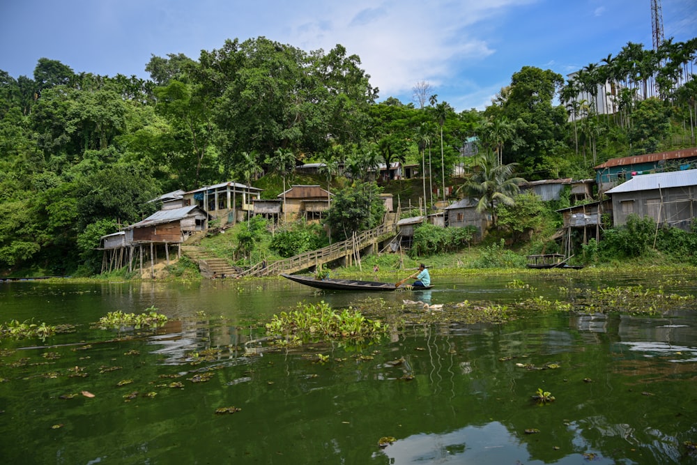 a person in a boat on a river with houses and trees
