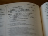 An open book showing a passage from Psalm 142, with text focused on themes of prayer and seeking assistance from the Lord. The book is positioned at an angle, and the lighting is soft, highlighting the text.