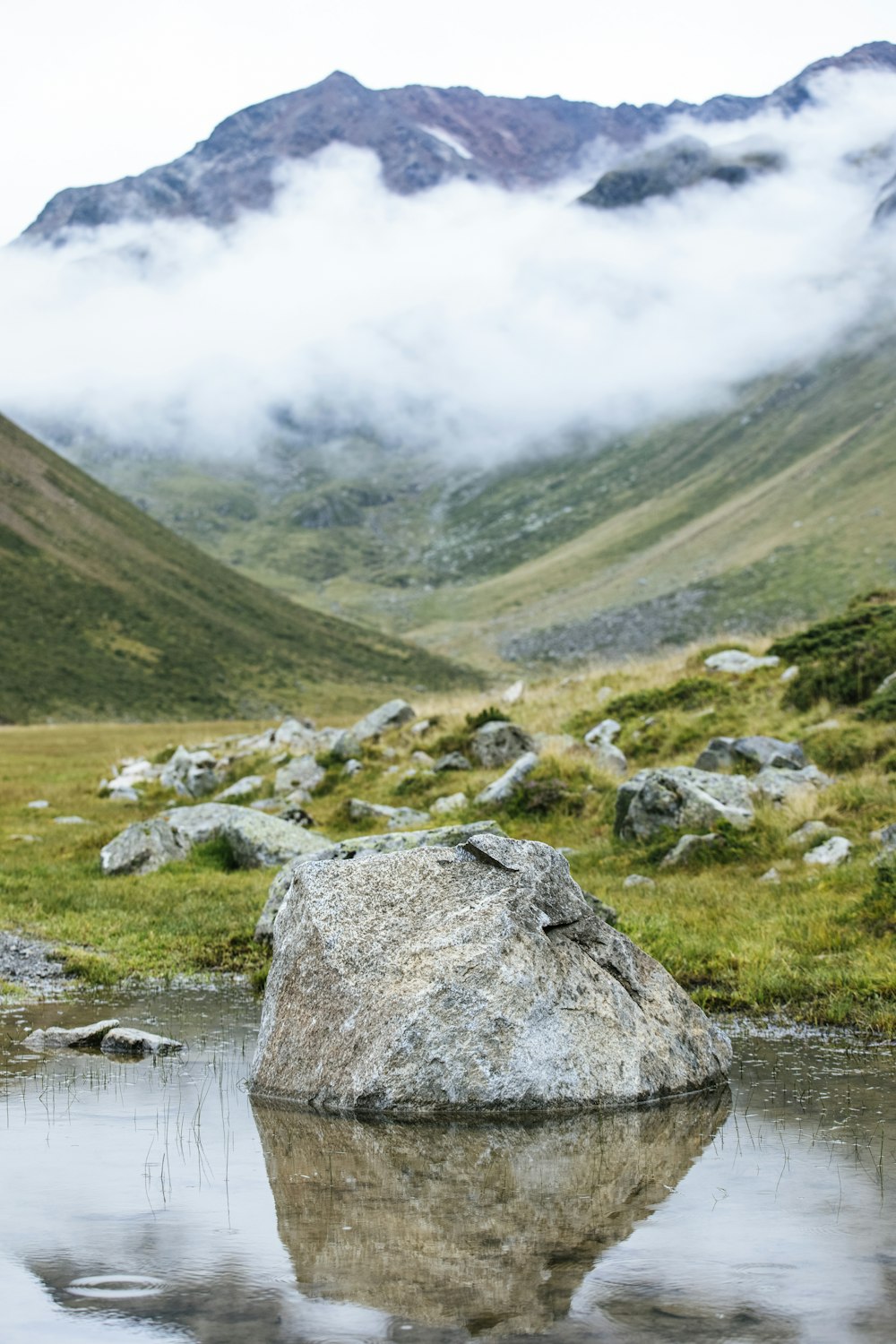 Ein großer Felsen in einem Gewässer mit Bergen im Hintergrund