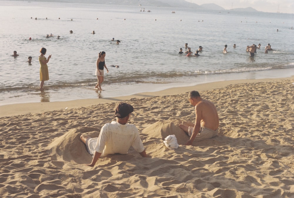 Una coppia di uomini seduti su una spiaggia con persone in acqua