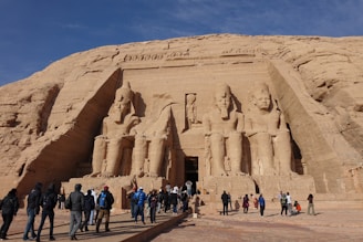 A group of travelers marveling at the ancient temples carved into the cliffs at Abu Simbel during golden hour.