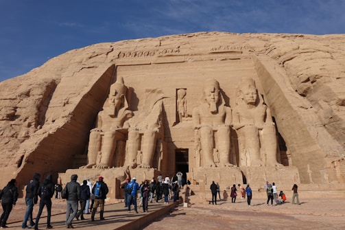 A group of travelers marveling at the ancient temples carved into the cliffs at Abu Simbel during golden hour.