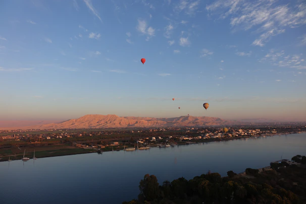 A serene drone shot showing emerald Nile river winding beneath softly glowing balloons at dawn.