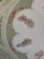 A beautifully painted ceiling features classical figures in flowing garments surrounded by ornate floral arrangements. The figures are depicted in dynamic poses, seemingly floating and carrying objects. The background showcases intricate ornamental designs enhancing the elegance of the scene.