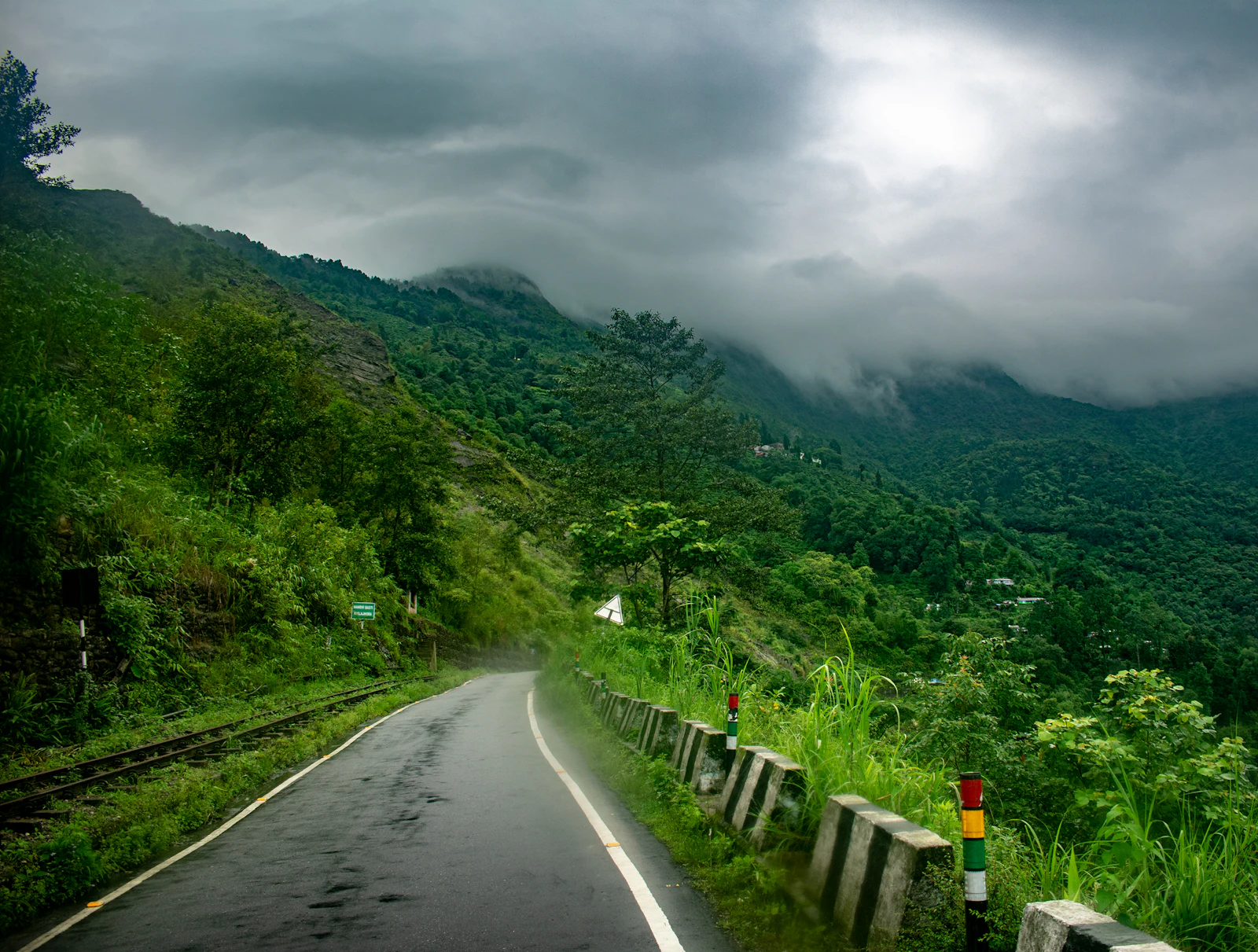 The hill road near Kurseong running beside the narrow toy train line under monsoon cloud