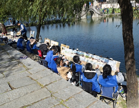 Children and adults collaborating on a nature-inspired art project by a riverside.