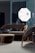 A modern interior setting featuring a stylish seating arrangement with a contemporary sofa, armchair, and a small table, all with sleek metal and dark fabric finishes. A large, illuminated photography umbrella is positioned behind the furniture, providing light and casting reflections on the shiny surfaces.