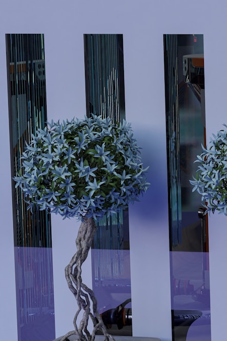 A decorative artificial tree with intricate twisted branches and lush foliage stands in front of sleek, reflective panels. The tree features a dense cluster of pale blue leaves and is complemented by the modern, stylish background.