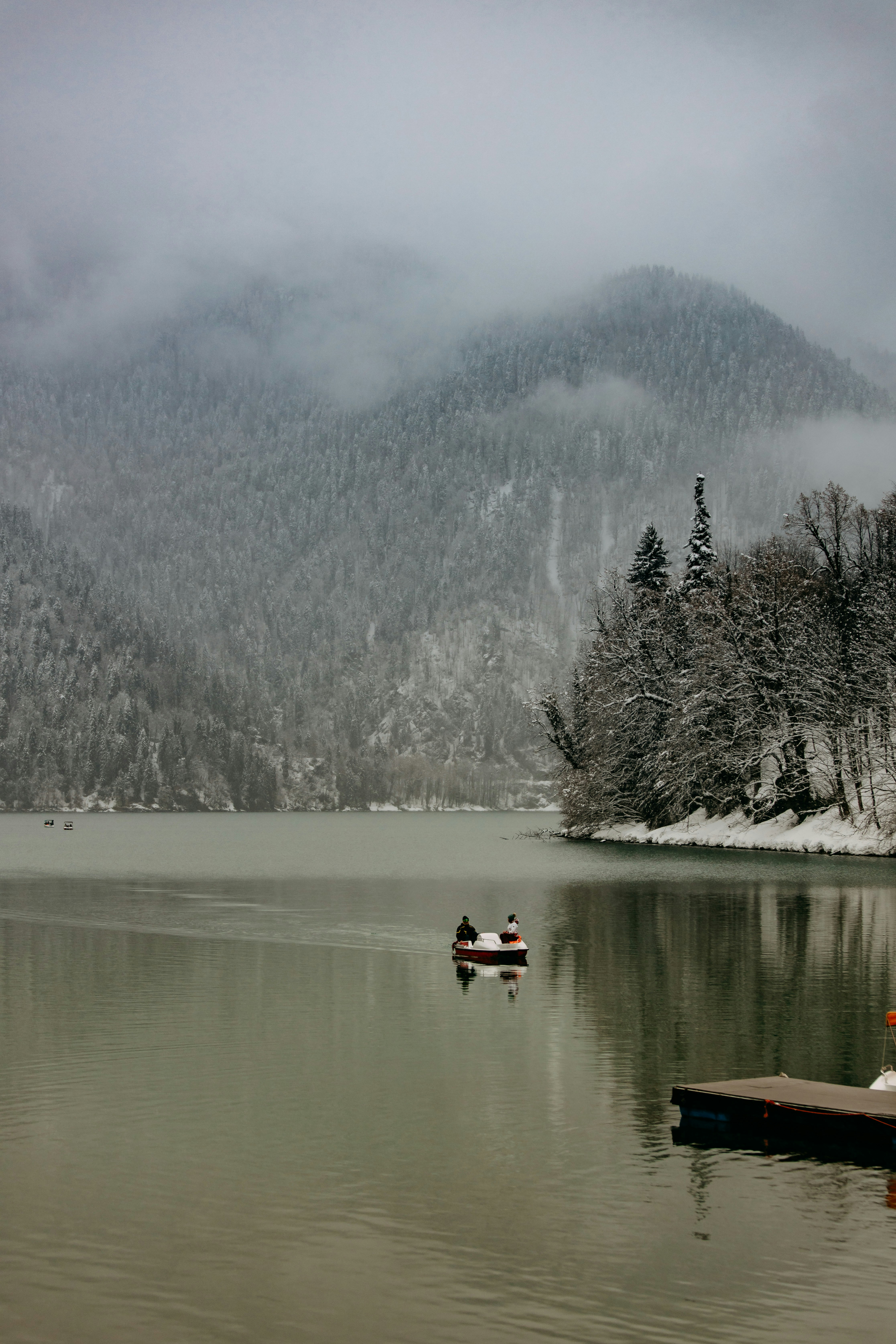 a group of people in a boat on a lake with trees and snow