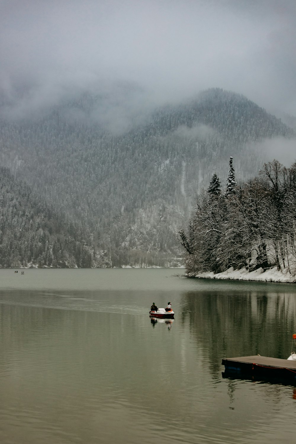 a group of people in a boat on a lake with trees and snow