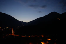 Evening view of the rural hotel with warm lights glowing amidst trees and mountains.