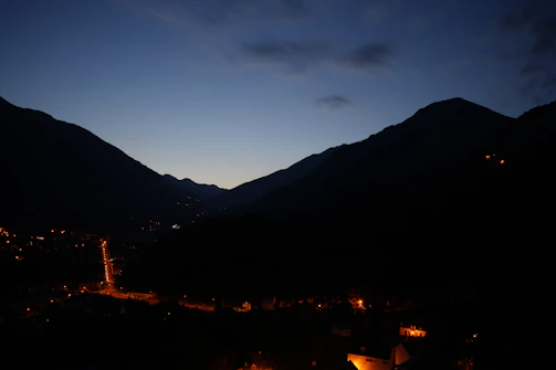 Evening street view showing warm lights of houses with mountain scenery in the background.