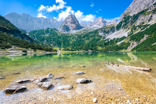 Lac de montagne turquoise au rivage de galets, versants verts et sommets rocheux
