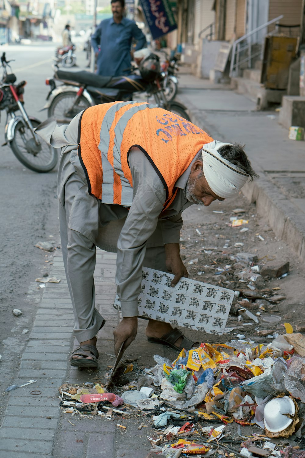 a person with a white hat and orange vest bending over to pick up trash