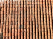 A repetitive pattern of weathered, red-brown roof tiles, arranged in neat rows, with visible wear and some areas of black discoloration and moss growth.