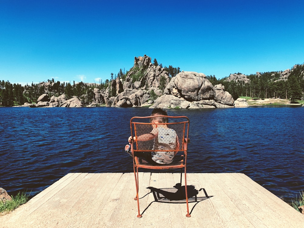 a person sitting in a chair on a dock by a body of water