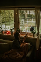 A peaceful scene of a model seated by a window, wrapped in a cozy, neutral-toned shawl.