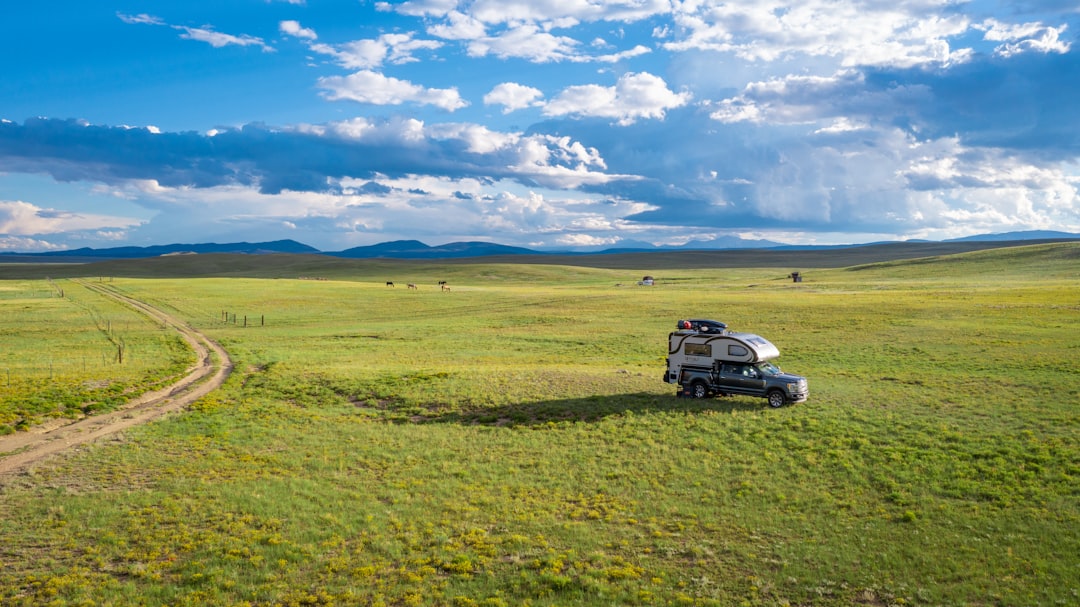 a car on a road in a field, RVing in summer in Colorado. Truck camper parked in a field surrounded by mountains and blue