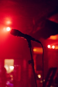 A solitary microphone is set up on a stand in a dimly lit space with red and orange ambient lighting, creating a warm and intimate atmosphere.