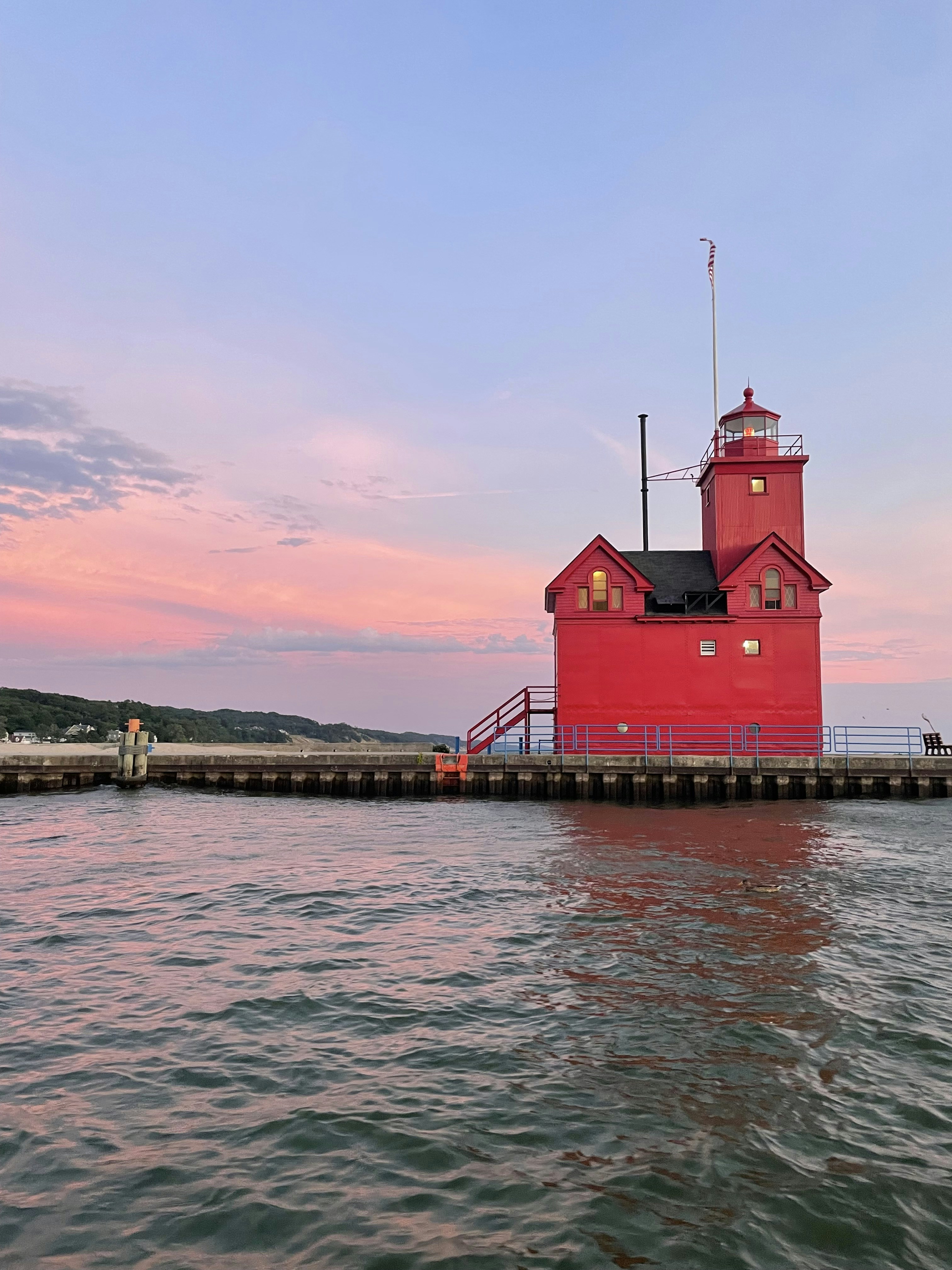 a red and white lighthouse on a dock with Holland Harbor Light in the background
