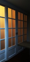 A set of sliding glass doors with a wooden frame, partially illuminated by a warm light from behind. The panels are arranged in a grid pattern, casting a soft glow through the translucent glass.