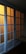 A set of sliding glass doors with a wooden frame, partially illuminated by a warm light from behind. The panels are arranged in a grid pattern, casting a soft glow through the translucent glass.