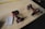 Two red cordless power drills are placed on a wooden surface along with a small spiral notebook containing handwritten numbers. A yellow measuring tape stretches across the table in the background.