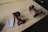 Two red cordless power drills are placed on a wooden surface along with a small spiral notebook containing handwritten numbers. A yellow measuring tape stretches across the table in the background.