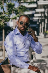 a man wearing sunglasses and a blue shirt sitting on a bench