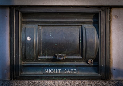 A secure metal box embedded into the wall, labeled 'Night Safe.' It has a sturdy and slightly worn appearance, with evident use and weathering.