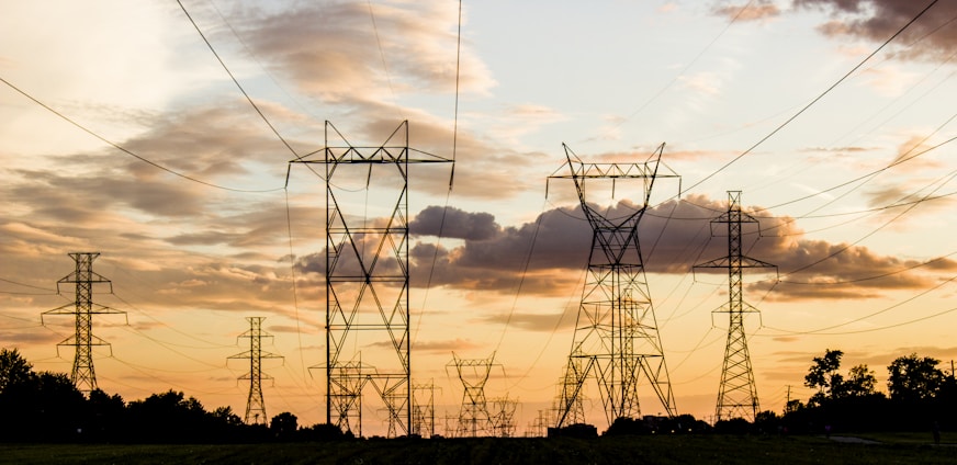 A panoramic view of a bustling power grid with transmission lines stretching across a vibrant American landscape at sunset.