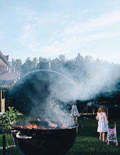 Happy family enjoying a barbecue in a sunny backyard with Six Boi meat packages on the table.