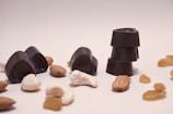 Several pieces of dark chocolate, shaped like hearts and circles, are arranged with various nuts and raisins scattered around them on a plain surface.