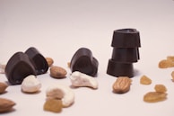 Several pieces of dark chocolate, shaped like hearts and circles, are arranged with various nuts and raisins scattered around them on a plain surface.