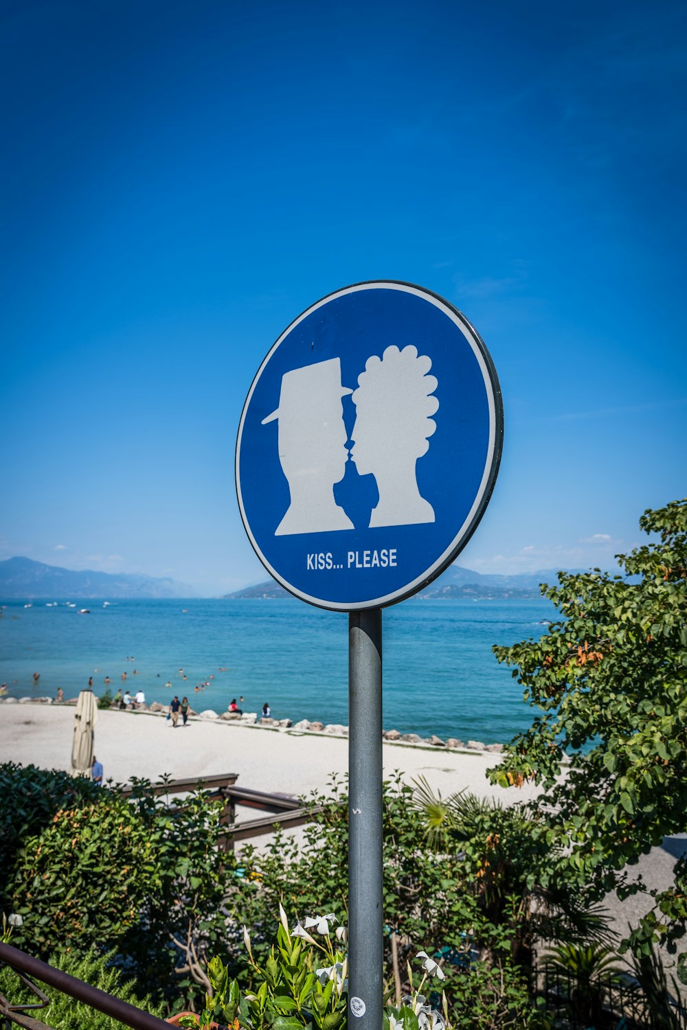 a sign on a pole with a beach and water in the background