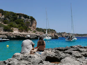a man and woman sitting on rocks looking at a body of water