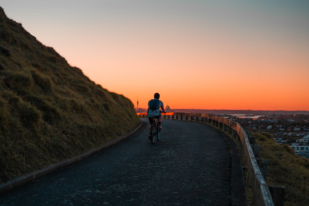 a person riding a bicycle on a road with a sunset in the background