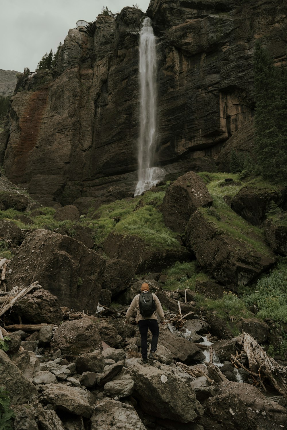 滝を背景に岩だらけの丘の中腹に立っている人
