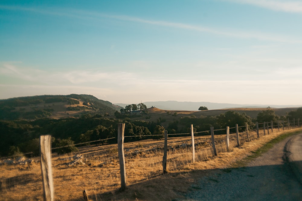 a fenced off field with a dirt road and hills in the background