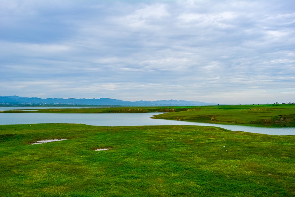 a large green field with a body of water in the background