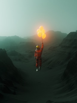 An astronaut with a bright orange suit is holding glowing yellow balloons. They are floating above a dark, rugged landscape with hills and a foggy, greenish sky.