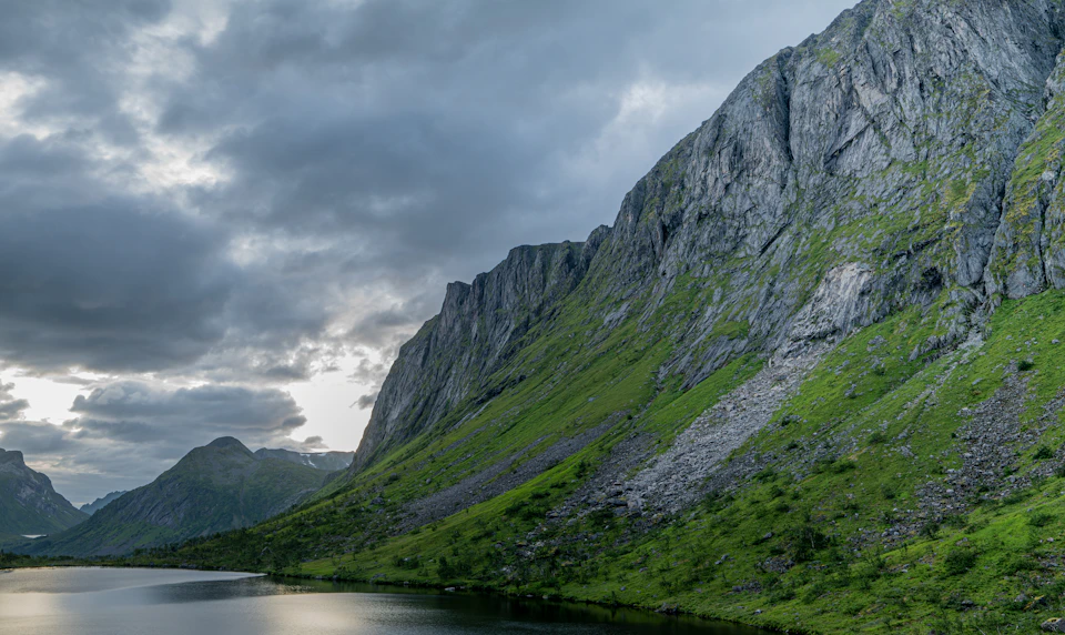 Serene mountain landscape features a large, jagged cliff face rising above a deep blue lake