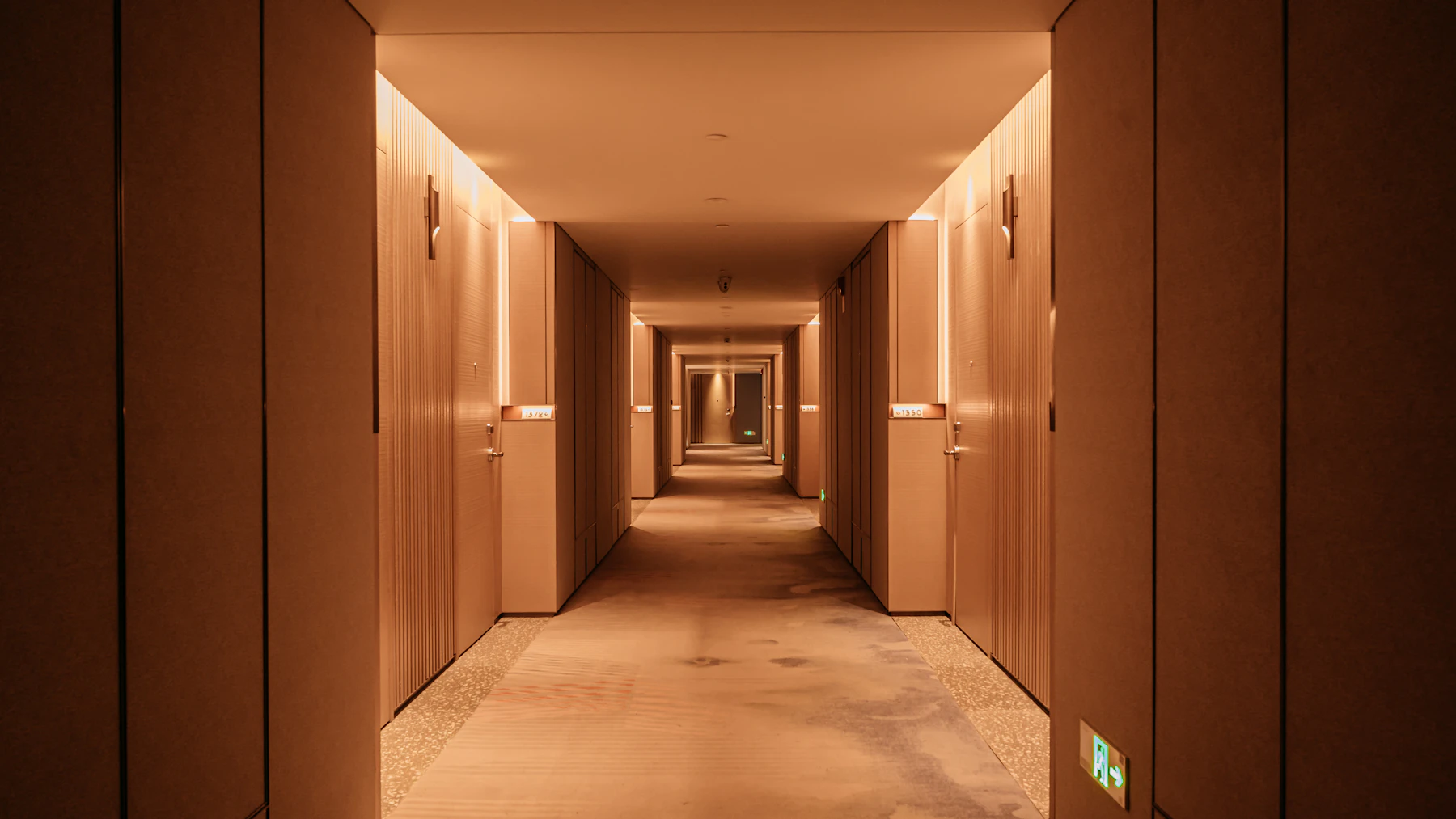 A lit hotel corridor extends past several closed room doors.