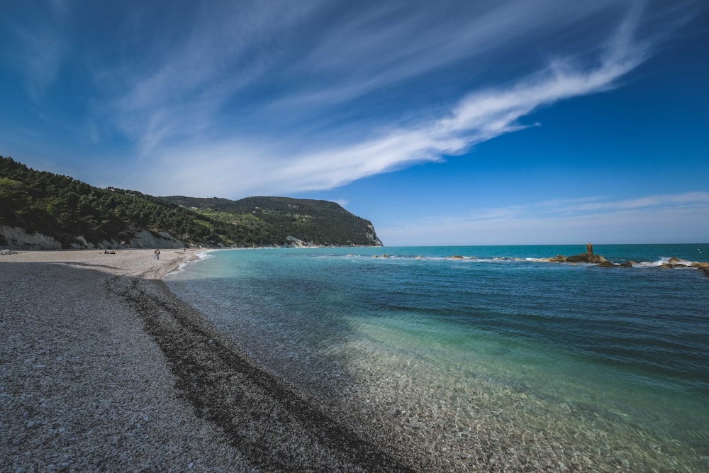 a beach with blue water and a hill in the background