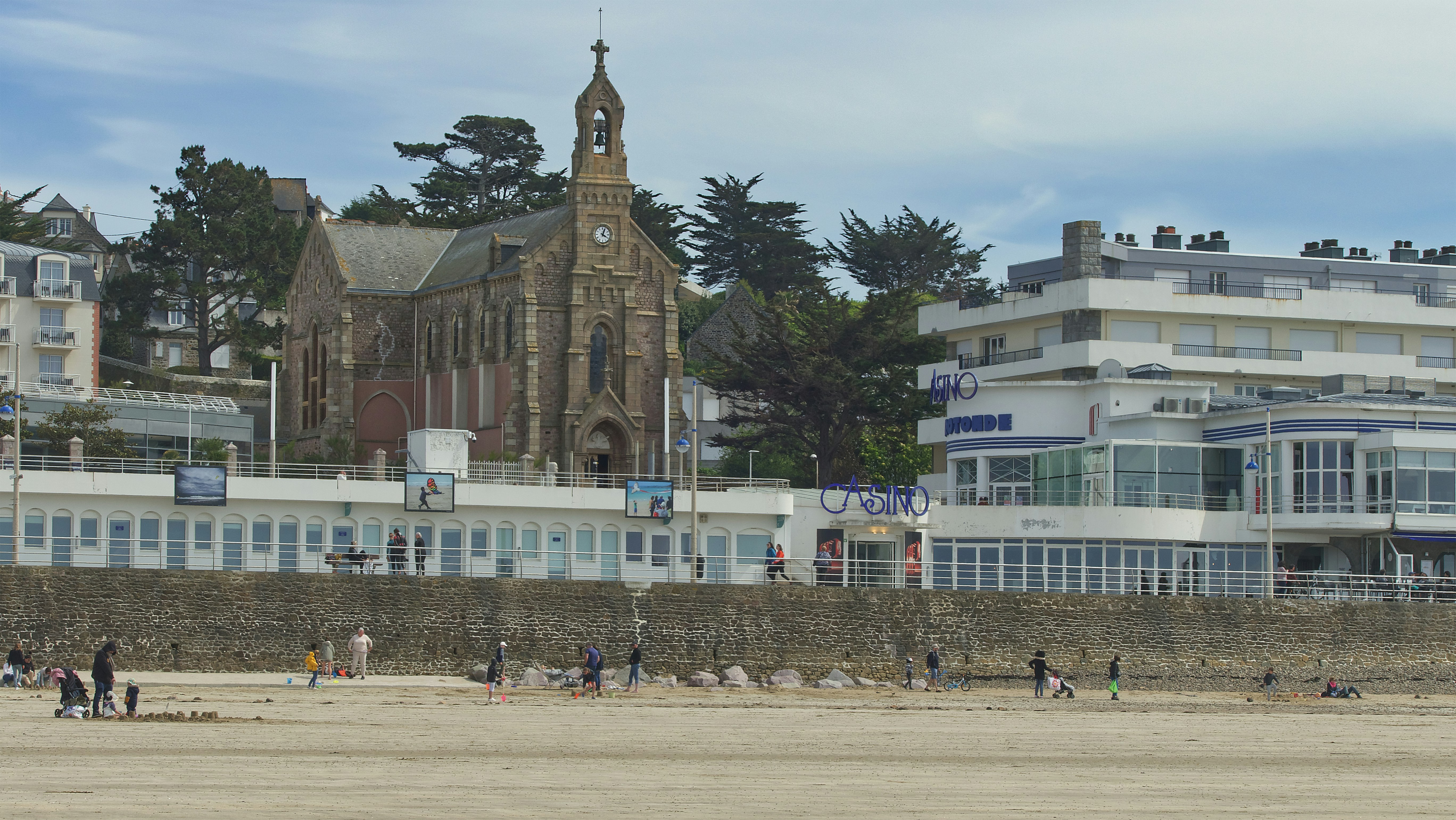 a group of people on a beach, Une balade sur la plage Val-André avec vue sur la Chapelle et le Casino.
