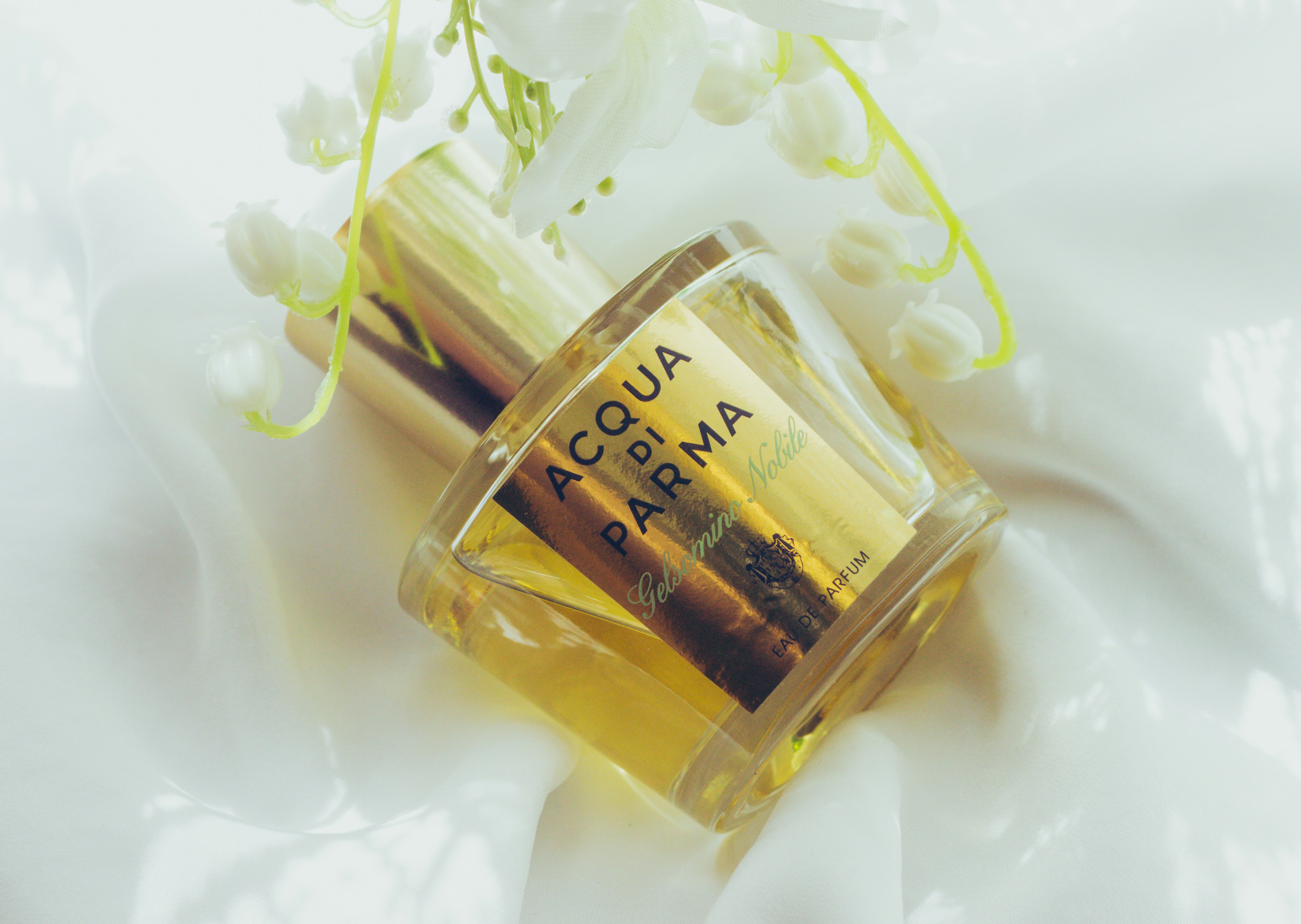 Feminine perfume bottle surrounded by silk fabric, soft golden light, romantic luxury atmosphere, high fashion fragrance photography