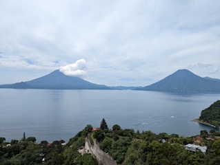 A panoramic view of Lake Atitlán with volcanoes rising in the background under a bright blue sky.