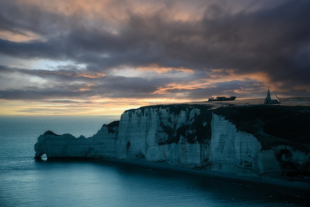 a rocky cliff with a body of water below with White Cliffs of Dover in the background