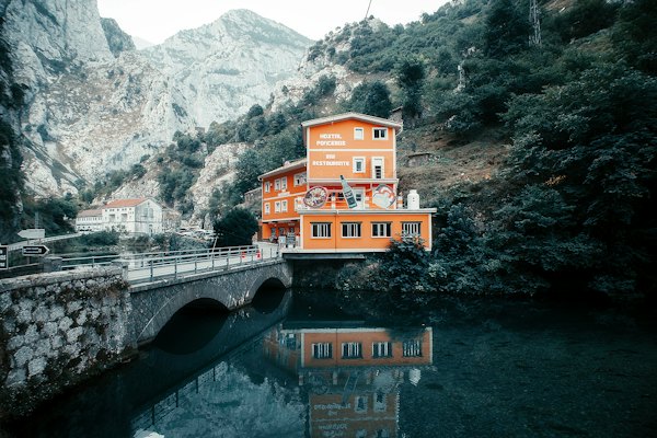 A house beside a bridge over a green river pool — Picos de Europa, Spain