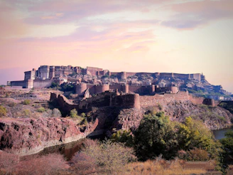 An ancient fort perched on a rocky hill, overlooking a serene desert landscape at sunset.